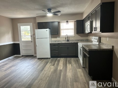 A kitchen with a white refrigerator, black cabinets, and a wooden floor.