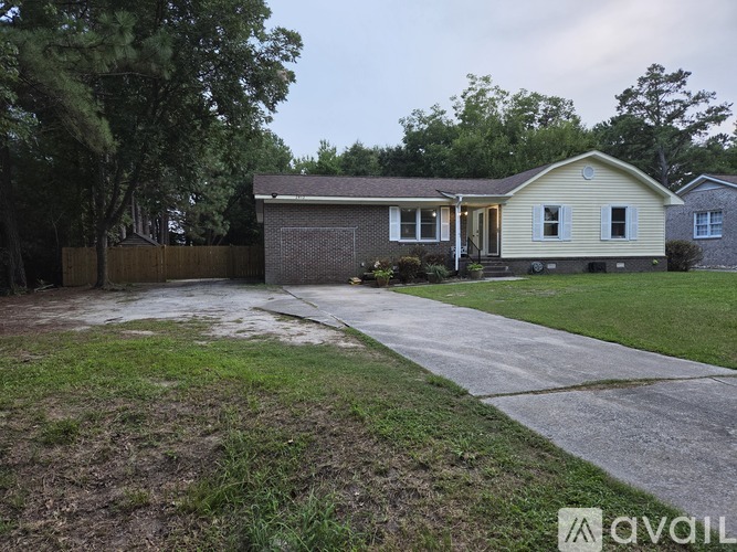 A house with a grey roof and a yellow exterior is surrounded by a fence and trees.