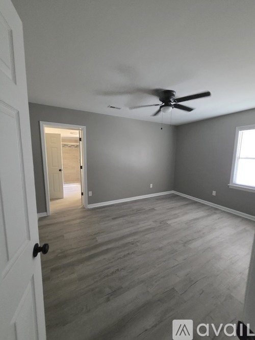 A room with a ceiling fan and light, hardwood floors, and a window.