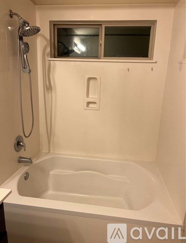 A white bathtub with a shower head and a window above it.