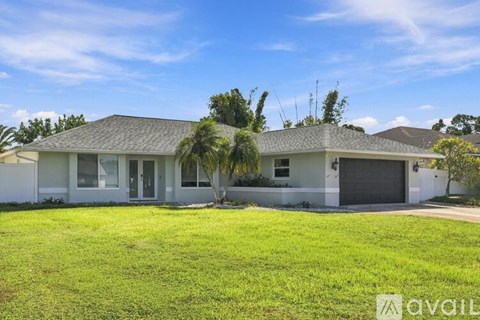A house with a white exterior and a grey roof is surrounded by a green lawn.