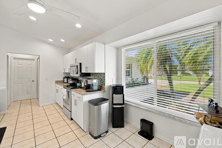 A kitchen with white cabinets and a black trash can.
