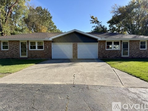 A two-story house with a garage is surrounded by a driveway and trees.