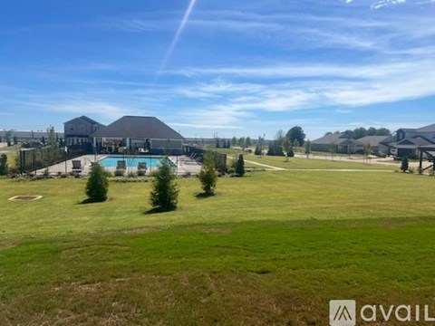 A large grassy field with a pool and a house in the background.