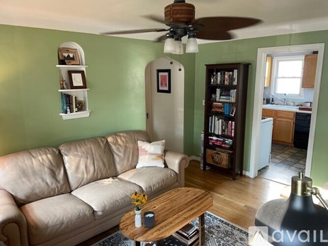 A living room with a tan couch, a coffee table, a ceiling fan, and a bookshelf.