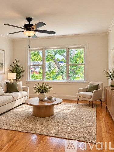 A living room with a white sofa, a coffee table, a ceiling fan, and a large window with a view of trees.