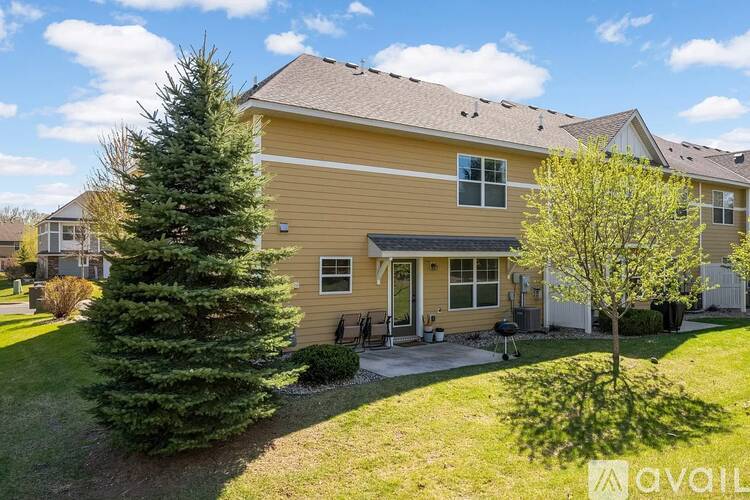 A house with a yellow exterior and a brown roof with a tree in front of it.