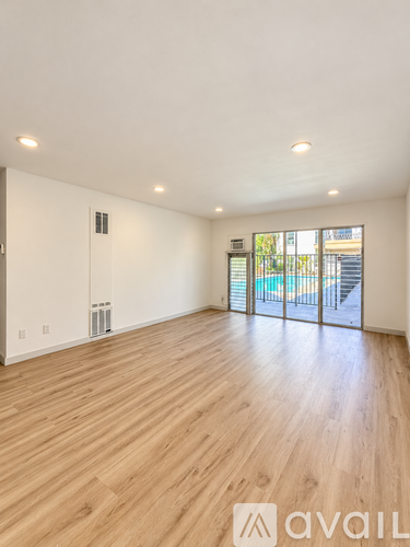 A spacious room with wooden flooring and a sliding glass door leading to a balcony.