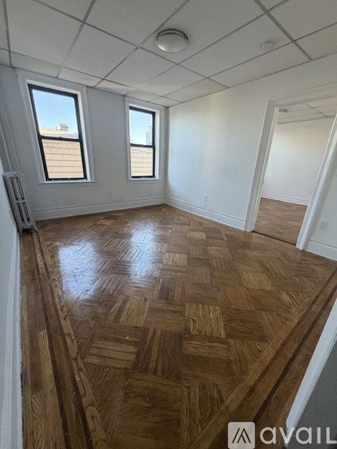 A room with wooden flooring and two windows.