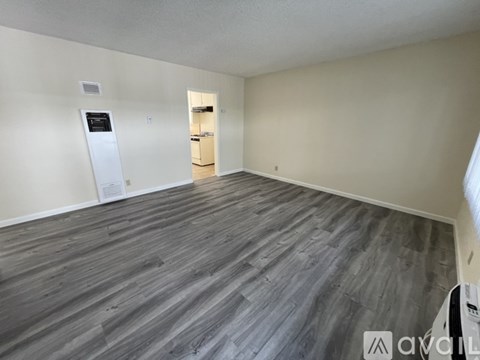 A spacious room with wooden flooring and a white wall.