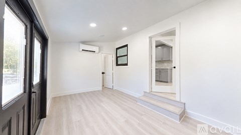 A spacious room with wooden flooring and a large window on the left.