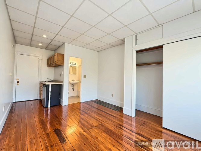 A room with wooden floors and white walls, with a door on the left and a closet on the right.