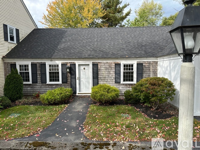 A small house with a white door and windows surrounded by bushes and a lamp post.