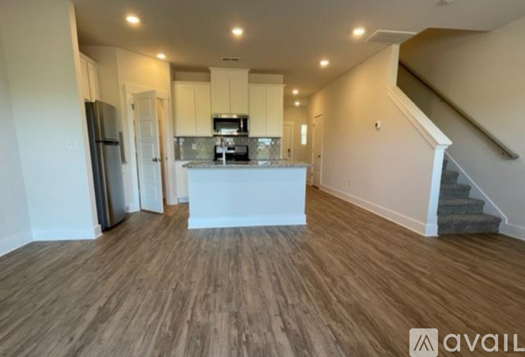 A spacious kitchen with wooden flooring and a staircase on the right side.