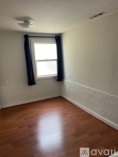 A room with wooden floors and a window with black curtains.