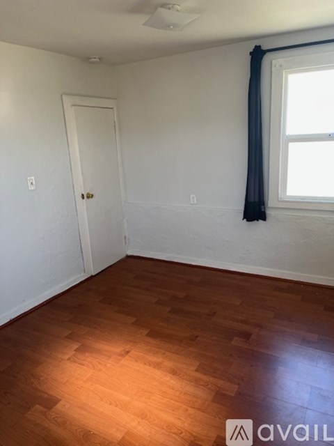 A room with wooden flooring and a window with a black curtain.