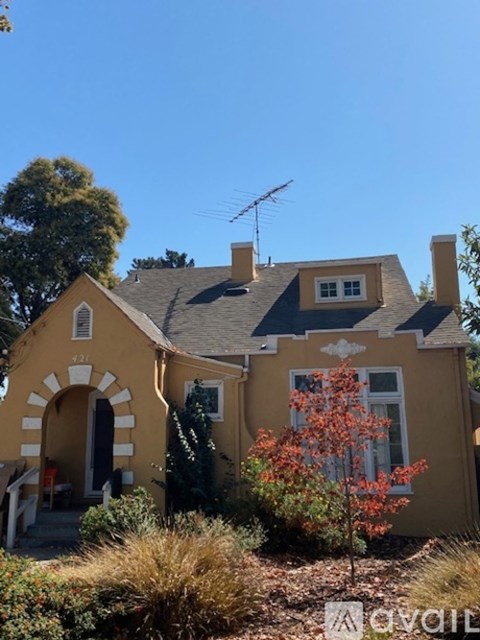 A yellow house with a black roof and a red tree in front.