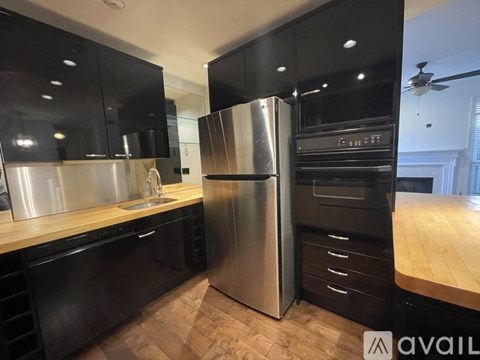 A modern kitchen with black cabinets and a stainless steel refrigerator.