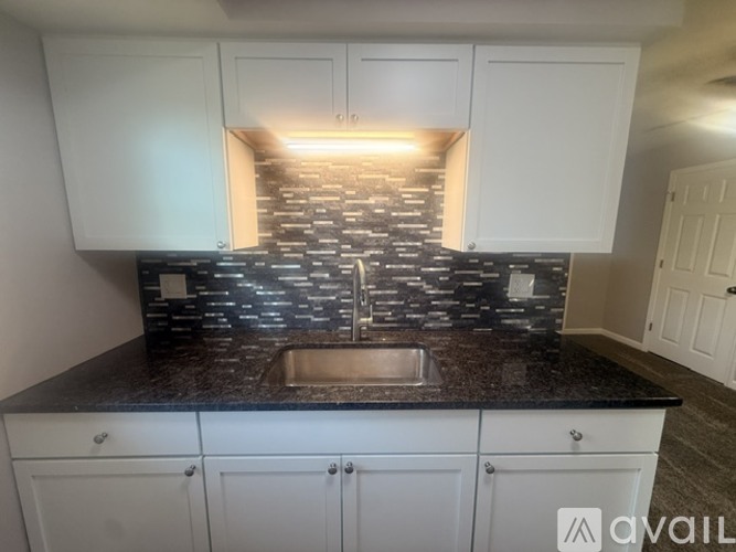 A kitchen with white cabinets and a black countertop with a sink.