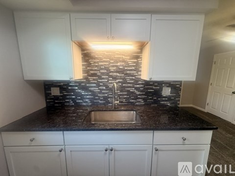 A kitchen with white cabinets and a black countertop with a sink.