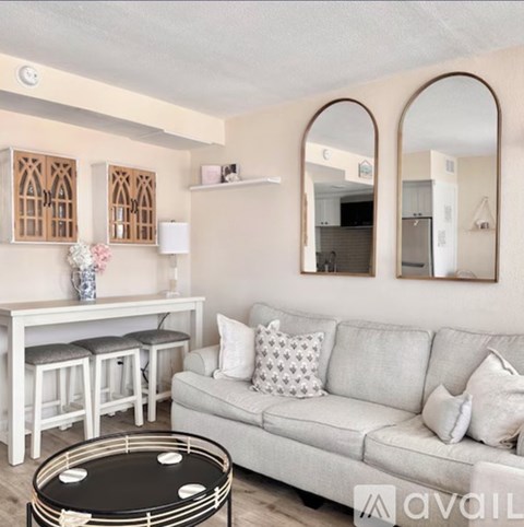 A living room with a grey couch, a black coffee table, and a white table with bar stools.