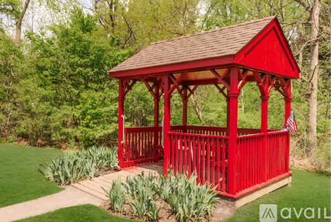 A red wooden gazebo with a brown roof is surrounded by greenery.