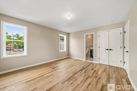 A room with wooden floors and a window showing a view of a street with cars and trees.