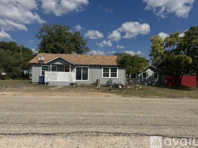 A house with a grey roof and white fence is in front of a tree.
