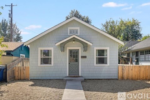 A small white house with a green roof and a wooden fence.
