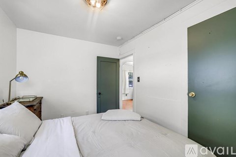 A bedroom with a bed, lamp, and a door leading to another room.