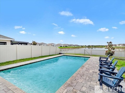 A pool surrounded by a white fence and blue lounge chairs.