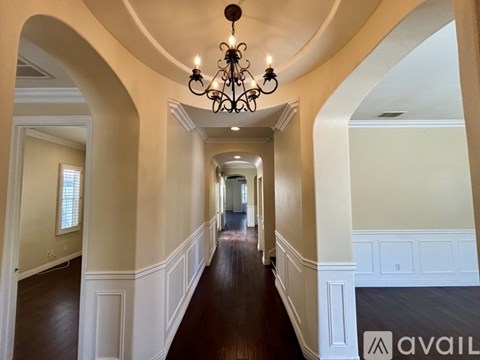 A long hallway with a chandelier and arched doorways.