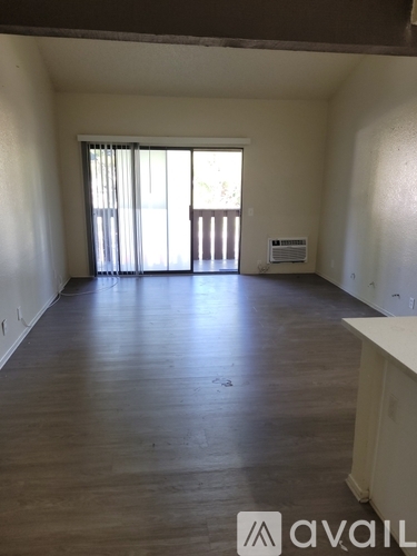 A spacious room with wooden floors and a large window with blinds.