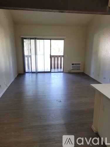 A spacious room with wooden floors and a large window with blinds.