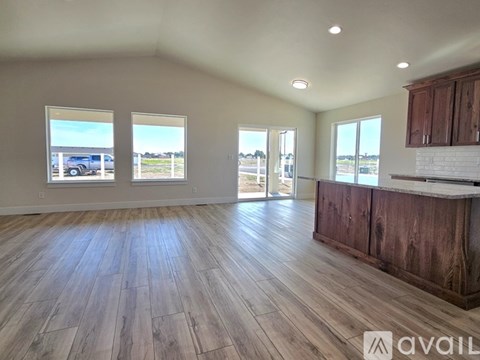 A spacious room with wooden flooring and a large window overlooking a parking lot.