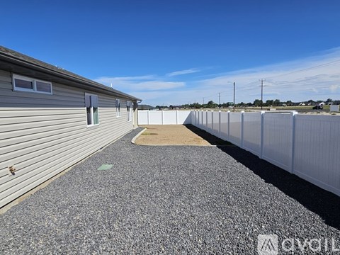 A gravel area in front of a grey building with a fence on the right side.