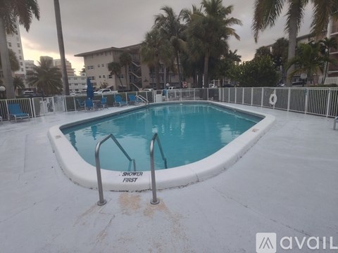 A pool with a sign that says "Shower First" is surrounded by palm trees.