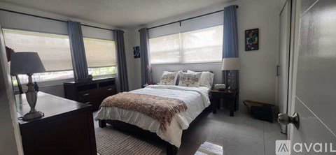 A bedroom with a large bed, a nightstand, and a window with blinds.
