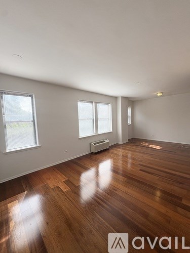 A room with wooden floors and white walls, with a window on the left side.