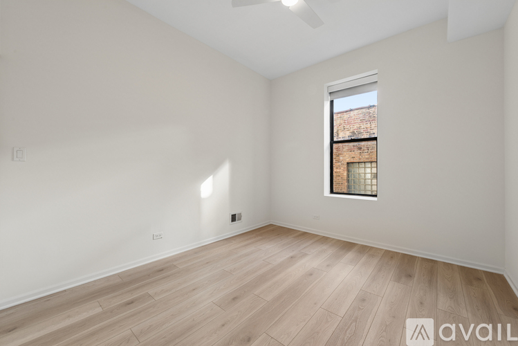 A room with wooden flooring and a window showing a brick building outside.