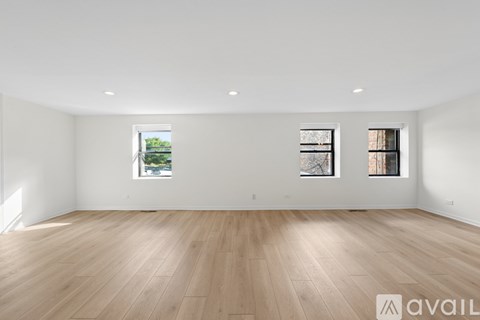 A spacious room with wooden flooring and two windows.