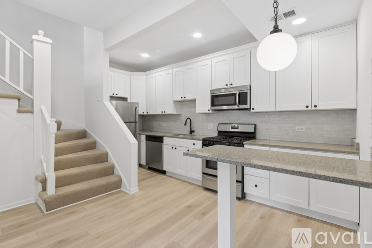 A modern kitchen with white cabinets and a staircase leading to the upper floor.