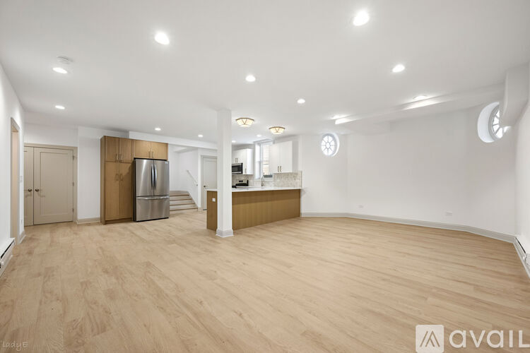 A spacious room with wooden flooring and a kitchen area in the background.