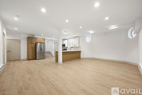 A spacious room with wooden flooring and a kitchen area in the background.