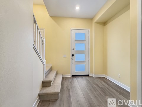 A hallway with a white door, stairs, and wooden flooring.