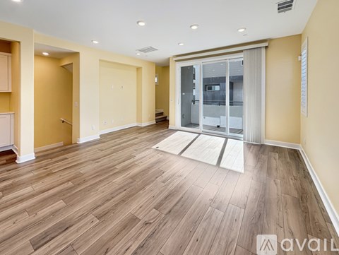 A spacious room with wooden flooring and a glass door leading to a balcony.