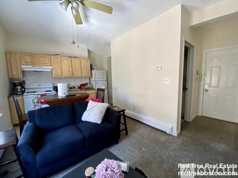A living room with a blue couch and a kitchen area in the background.