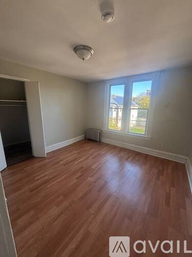 A room with wooden flooring and a window overlooking a fence.