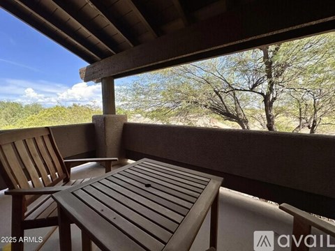 A wooden chair and table are on a patio overlooking a tree.