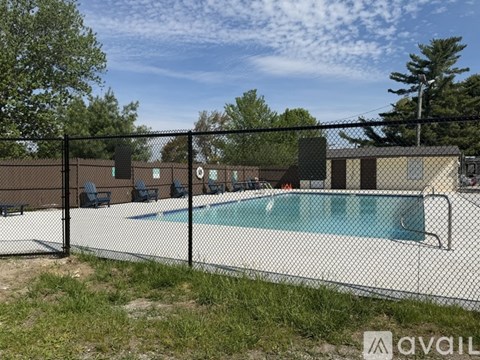 A pool surrounded by a black fence with chairs and trees in the background.